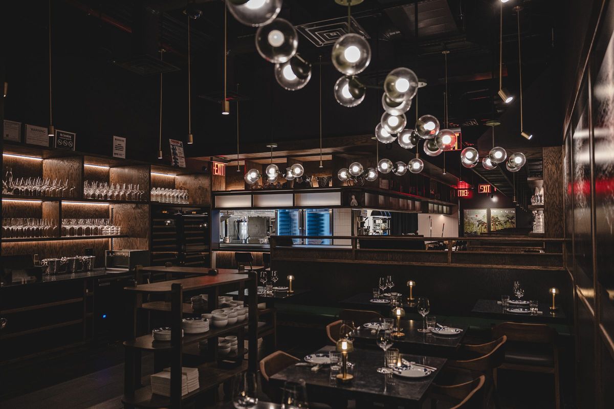 Dining tables beneath a cluster of glass globe pendants, lit glass shelving behind, Jeju Noodle Bar.