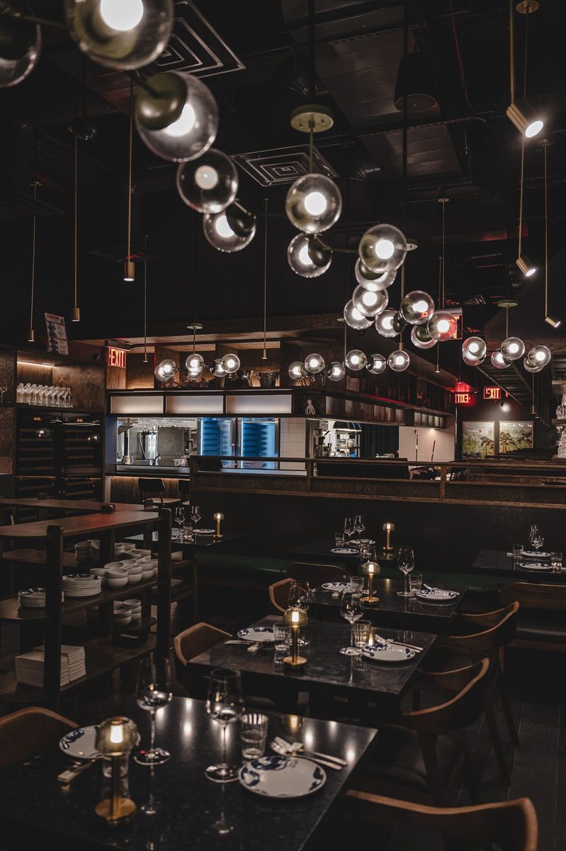 Dining room under clustered globe pendants with brass table lamps, Jeju Noodle Bar.