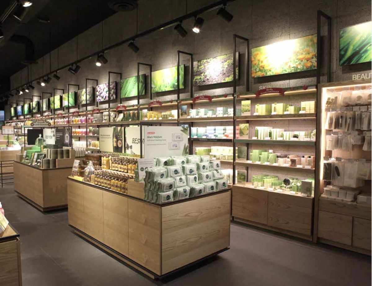 Retail floor with white-oak casework, open display islands and lit wall shelving, Nature Republic.